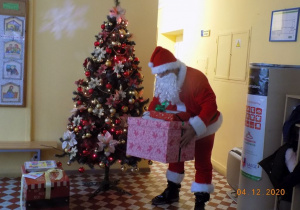 Mikołaj kładzie prezenty pod choinkę.