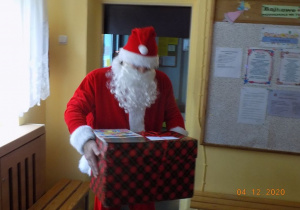 Mikołaj wnosi prezent do przedszkolnego holu.
