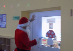 Mikołaj macha przez drzwi do dzieci z grupy muchomorków.