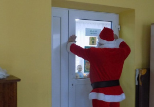 Mikołaj macha przez drzwi do dzieci z grupy skrzatów.