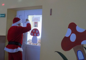 Mikołaj macha przez drzwi do dzieci z grupy muchomorków.