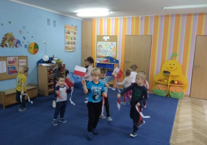 Dzieci z grupy pierwszej i trzeciej tańczą w kole i machają flagami Polski