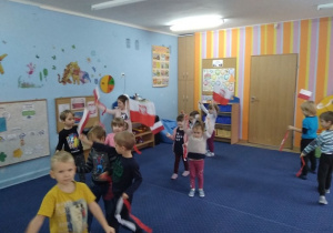 Dzieci z grupy pierwszej i trzeciej tańczą w kole i machają flagami Polski