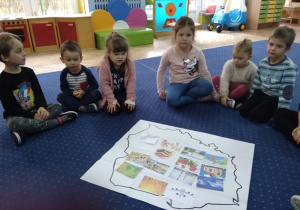 Dzieci siedzą w kole przy mapie Polski