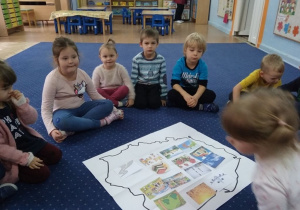 Dzieci siedzą w kole i oglądają mapę Polski