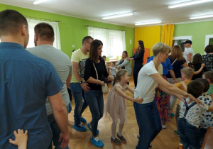 Dzieci z rodzicami i nauczycielkami bawią się na sali gimnastycznej