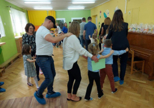 Dzieci z rodzicami i nauczycielkami bawią się na sali gimnastycznej