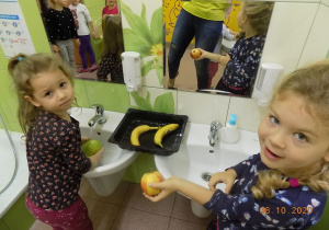 Dziewczynki myją owoce w umywalce.
