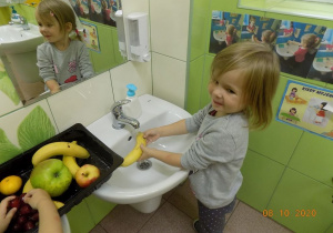 Dziewczynka myje owoce w umywalce.