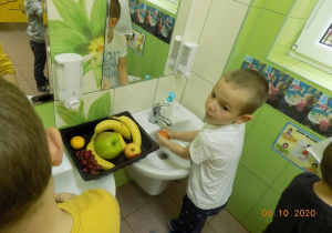 Chłopiec myje owoce w umywalce.