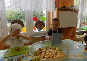 Dzieci w czapkach i fartuszkach kucharskich kroją owoce.
