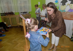 Nauczycielka gratuluje dziecku i wręcza książkę.