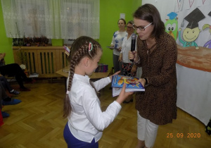 Nauczycielka gratuluje dziecku i wręcza książkę.