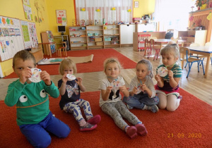 Dzieci siedzą na dywanie i pokazują ordery przedszkolaka.