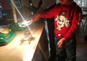 Chłopiec trzyma w ręku lampę i zbliża ją do samochodziku z małym panelem słonecznym