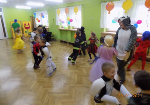 Dzieci w strojach karnawałowych tańczą na sali gimnastycznej podczas balu.