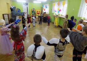 Dzieci w strojach karnawałowych tańczą na sali gimnastycznej podczas balu.