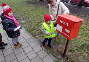 Chłopiec wkłada list do skrzynki pocztowej.