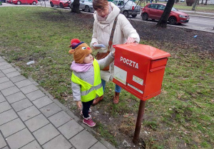 Dziewczynka wkłada list do skrzynki pocztowej.