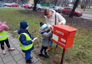 Chłopiec wkłada list do skrzynki pocztowej.