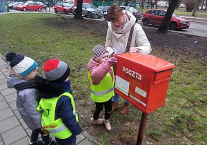 Dziewczynka wkłada list do skrzynki pocztowej.