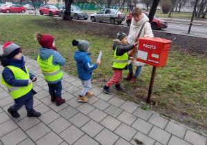 Dzieci stoją w kolejce do skrzynki pocztowej.