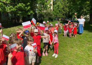 Dzieci maszerują z flagami Polski po ogrodzie