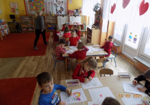 Dzieci siedzą przy stołach i kolorują obrazek konturowy czerwony kapturek.