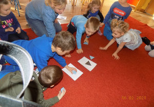 Dzieci siedzą na dywanie i układają wzory z niebieskiej mozaiki geometrycznej.