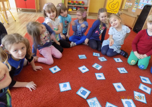 Dzieci siedzą w kole na dywanie i grają w niebieskie memory.