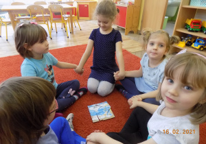 Dzieci siedzą w małych kółeczkach trzymając się za ręce, pośrodku leżą ułożone puzzle - smerfy.