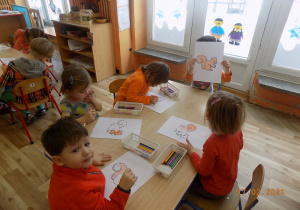 Dzieci siedzą przy stole i kolorują obrazek konturowy wiewiórkę.