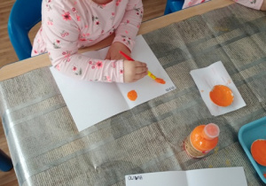 Dzieci z grupy I malują pędzlem kleksy z pomarańczowej farby