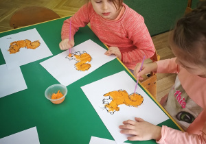Dzieci z grupy trzeciej malują pomarańczową farbą wiewiórkę.