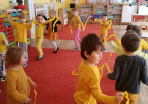 Dzieci tańczą po kole trzymając paski żółtej bibuły.