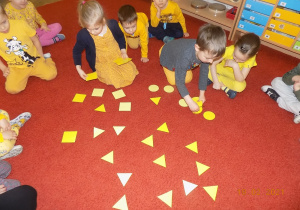 Dzieci układają na dywanie żółte koła, trójkąty i kwadraty.