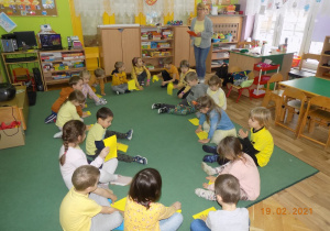 Dzieci z grupy trzeciej siedzą w kole i trzymają w ręku żółtą kartkę.