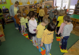 Dzieci z grupy trzeciej chodzą po kolorowych kartkach w rytm muzyki.