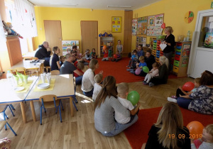 Dzieci i rodzice z grupy drugiej siedzą na dywanie z balonami, przygotowują się do zabawy. Pani Dyrektor przemawia do rodziców