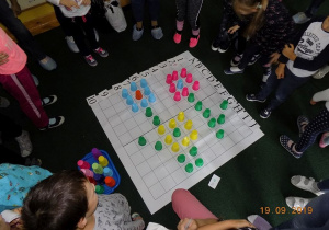 Dzieci rodzice z grupy czwartej oglądają wzór, jaki wyszedł z kolorowych kubków na macie do kodowania