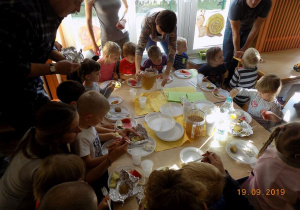 Dzieci korzystają z poczęstunku po zabawach, siedzą przy stole i zajadają zdrowe przekąski