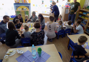 Dzieci w grupie pierwszej siedzą przy stole i jedzą owoce i warzywa, popijają sokiem
