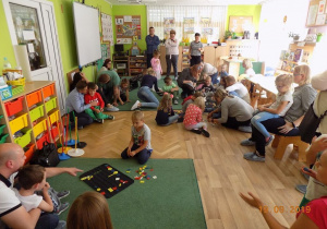 Dzieci i rodzice z grupy czwartej układają na dywanie mozaikę geometryczną