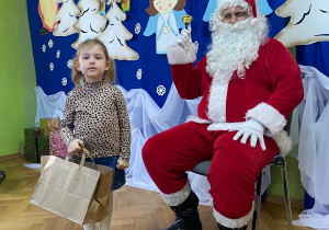 Dziewczynka stoi obok Mikołaja z prezentem