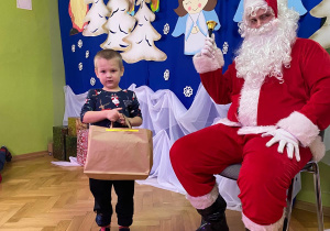 Chłopiec stoi obok Mikołaja z prezentem