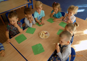Dzieci z grupy pierwszej siedzą przy stole i jedzą banany