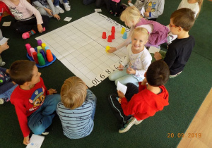 Dzieci z grupy czwartej układają wzór z kolorowych kubków na macie do kodowania