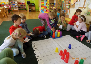 Dzieci z grupy czwartej układają wzór z kolorowych kubków na macie do kodowania