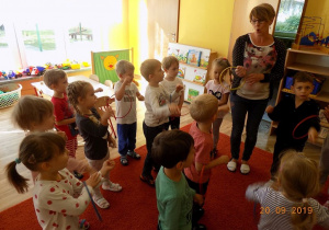 Pani Marlena z grupy dgrugiej pokazuje dzieciom, jak nakładać obręcz na rękę