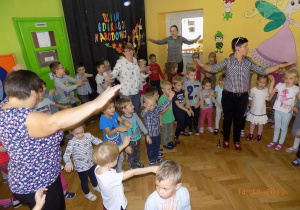 Dzieci i pracownicy przedszkola tańczą w kole z wyciągniętymi do przodu rękami